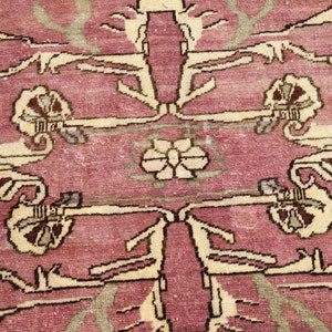 May include: A vintage rug with a pink background and a cream-colored floral pattern. The rug has a worn and faded look, giving it a unique character.