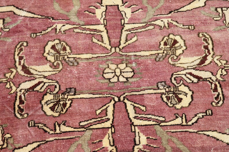 May include: A vintage rug with a pink background and a cream-colored floral pattern. The rug has a worn and faded look, giving it a unique character.