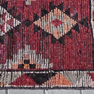 Puede incluir: Primer plano de una alfombra roja, negra y blanca con un borde de flecos. La alfombra tiene un dise&ntilde;o geom&eacute;trico con formas de diamante.
