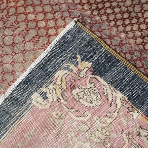 May include: Close-up of a corner of a vintage rug with a dark blue border and a pink and cream floral design. The rug has a geometric pattern in red and brown.