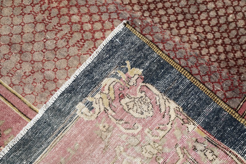 May include: Close-up of a corner of a vintage rug with a dark blue border and a pink and cream floral design. The rug has a geometric pattern in red and brown.