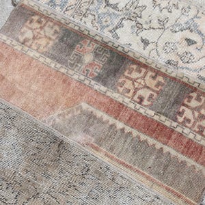 May include: A section of a vintage rug with a patchwork design. The rug features a mix of colors, including beige, red, and gray, with intricate patterns and a distressed appearance. The rug is placed on a stone surface.