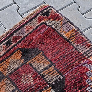 Puede incluir: Una alfombra roja, naranja y negra con un patr&oacute;n y un borde con flecos. La alfombra est&aacute; hecha de lana tejida y tiene un dise&ntilde;o tradicional.