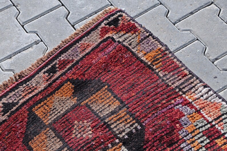 Puede incluir: Una alfombra roja, naranja y negra con un patr&oacute;n y un borde con flecos. La alfombra est&aacute; hecha de lana tejida y tiene un dise&ntilde;o tradicional.
