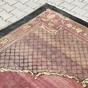 May include: A vintage rug with a geometric pattern in shades of red, brown, and beige. The rug has a black border and a faded appearance.