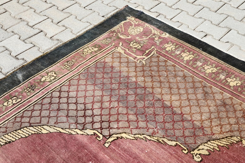 May include: A vintage rug with a geometric pattern in shades of red, brown, and beige. The rug has a black border and a faded appearance.