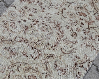 May include: A vintage rug with a cream background and a brown floral pattern. The rug has a distressed look and is made of a soft, woven material.