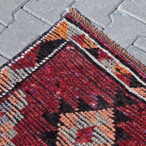 Puede incluir: Una alfombra roja, negra y blanca con un borde de flecos. La alfombra tiene un dise&ntilde;o geom&eacute;trico con una variedad de colores y texturas.