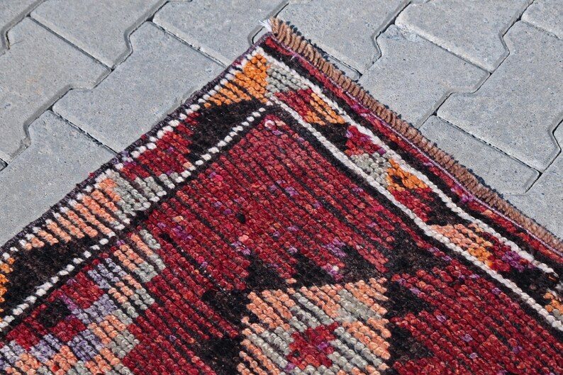 Puede incluir: Una alfombra roja, negra y blanca con un borde de flecos. La alfombra tiene un dise&ntilde;o geom&eacute;trico con una variedad de colores y texturas.