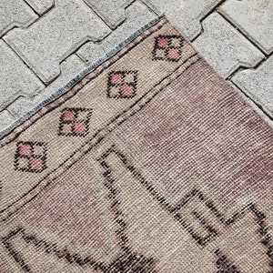 May include: A vintage pink and beige rug with a geometric pattern. The rug has a fringe border and is made of wool.