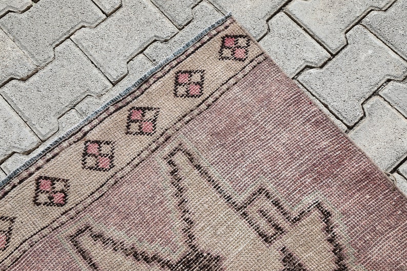 May include: A vintage pink and beige rug with a geometric pattern. The rug has a fringe border and is made of wool.