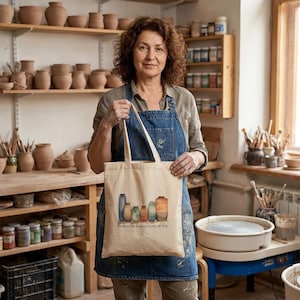 May include: A woman in a pottery studio holds a beige tote bag with a watercolor illustration of vases. The bag has the text "We have the treasures in jars of clay." Shelves of pottery and jars are in the background.