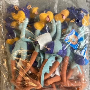 May include: A clear plastic bag filled with plush Road Runner toys. The toys have blue, yellow, and orange features, with tags attached. The Road Runner has a long neck, legs, and tail, and is wearing a purple vest.