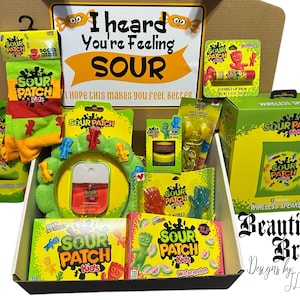 May include: A gift box filled with Sour Patch Kids merchandise. Includes candy, socks, a wireless speaker, and a sign that reads "I heard you're feeling sour." The box is decorated with yellow, green, and red accents.