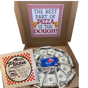 May include: A brown cardboard pizza box with a red and white checkered pattern. The box is open and contains a gift card and rolled up bills. The box has a sign on the front that says "The best part of pizza is the dough!"