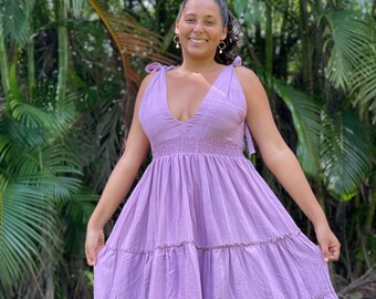 Puede incluir: Una mujer con un vestido maxi de color lavanda con volantes, escote en V profundo y tirantes finos. El vestido tiene una cintura fruncida y una falda fluida.