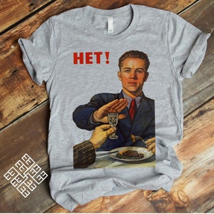 Puede incluir: Una camiseta gris con una impresión roja de un hombre que dice "HET!" mientras levanta la mano para detener a alguien que le da un vaso de alcohol. El hombre lleva un traje azul y una corbata roja.