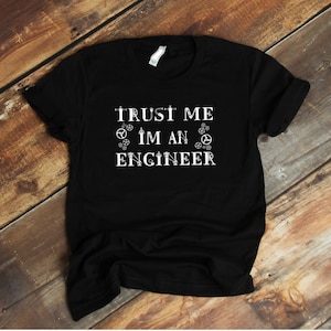 Peut inclure: T-shirt noir avec un texte blanc qui dit "Faites-moi confiance, je suis un ingénieur" avec de petites icônes d'engrenages autour du texte.