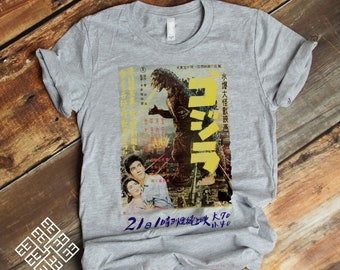 May include: A gray t-shirt with a vintage Japanese movie poster print featuring Godzilla, a giant monster, in a city scene. The poster text reads "水曜大怪獣映画" and "21日1時性統上映 k70 inyo".