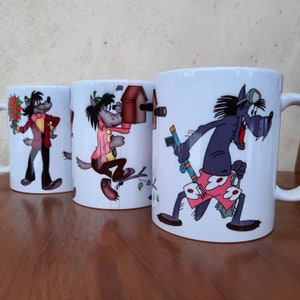 May include: Three white ceramic mugs with cartoon wolf illustrations. The mugs feature different scenes with the wolf character. One mug shows the wolf holding a flower, another shows the wolf building a birdhouse, and the third shows the wolf holding a water gun.