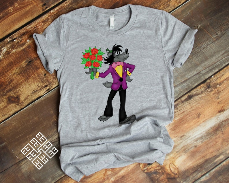 May include: A gray t-shirt with a cartoon wolf wearing a purple suit and holding a bouquet of red roses. The wolf is smiling and has a bow tie on.