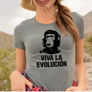 Op de afbeelding: Een grijs T-shirt met een zwart-witte afbeelding van een aap die een baret met een ster draagt. De tekst "VIVA LA EVOLUCIÓN" staat onder de afbeelding.