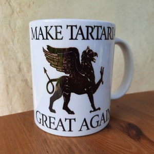 Könnte beinhalten: Eine weiße Keramiktasse mit einem schwarzen und goldenen Greifendesign und dem Text "MAKE TARTARIA GREAT AGAIN".