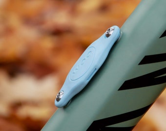 May include: A light blue plastic cover with a silver screw and the word "VCO" printed on it. The cover is attached to a green bike frame with black stripes.