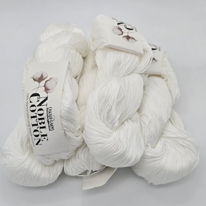Pode incluir: Vários novelos de fio Noble Cotton branco, cada um com uma etiqueta com o logotipo Cascade Yarns e as palavras "Noble Cotton" e "100% Mercerized Long Staple Cotton". Apresentado sobre um fundo branco.