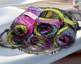 May include: A silver serving tray holds several skeins of colorful yarn. The yarn is a mix of purple, green, blue, and pink. The yarn is labeled with the brand name "Noro". The tray has ornate handles and a decorative edge.