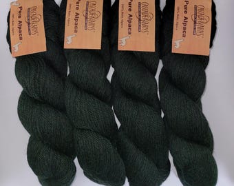 Puede incluir: Cuatro madejas de hilo verde bosque oscuro dispuestas una al lado de la otra. Cada madeja tiene una etiqueta de papel color canela con el texto Cascade Yarns, Pure Alpaca, 100% Baby Alpaca y un pequeño gráfico de una alpaca. El hilo es fibroso.