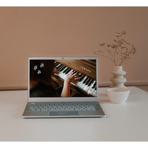 May include: A silver laptop computer with a white keyboard is open and displaying a video of a person playing a brown Yamaha piano. The video has white stars drawn on it.