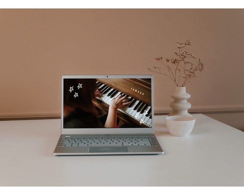 May include: A silver laptop computer with a white keyboard is open and displaying a video of a person playing a brown Yamaha piano. The video has white stars drawn on it.