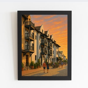 May include: Framed print depicting a street scene with buildings and people. The buildings are white with black balconies and dark roofs. The sky is a vibrant orange and yellow. People are walking on the cobbled street. The print is in a black frame.