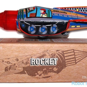 May include: A red, blue, and silver toy rocket with a friction powered mechanism. The rocket has a clear plastic bubble on top with a figure inside. The rocket is labeled "Space Commander" and is on a box that says "Rocket" and "Collector's Model".