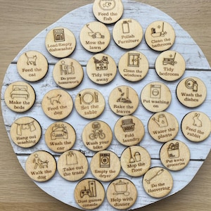 May include: A wooden chore chart featuring 28 circular wooden tokens. Each token is engraved with a different household task, including "Feed the fish," "Wash the car," and "Do the Hoovering." The tokens are arranged on a wooden plaque.
