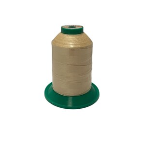 Pode incluir: Uma bobina de fio cor de creme em uma bobina de plástico verde. O fio está enrolado firmemente e está pronto para ser usado em uma máquina de costura.