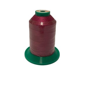 Pode incluir: Uma bobina de fio rosa em um carretel de plástico verde. O fio está enrolado firmemente e tem um leve brilho.