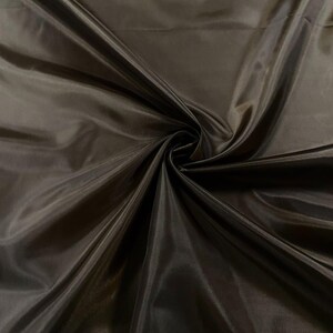 May include: A close-up of a smooth, dark brown fabric with a silky sheen. The fabric is draped and folded, creating soft curves and folds.