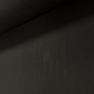 May include: A close-up shot of a dark, matte black surface. The texture appears smooth with subtle variations in tone and a diagonal shadow across the upper left corner. The overall impression is of a solid, uniform material.
