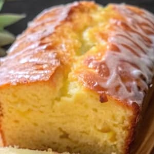 Op de afbeelding: Een citroencake in de vorm van een brood met een witte glazuur, gesneden op een houten snijplank.