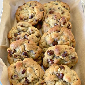 May include: A close-up of a baking dish filled with freshly baked chocolate chip cookies. The cookies are golden brown and have a slightly crispy exterior. They are arranged in a single layer, with some overlapping.