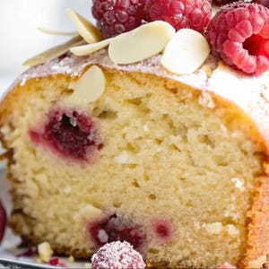 Puede incluir: Primer plano de una rebanada de pastel con glaseado blanco y virutas de almendras. El pastel está cubierto con frambuesas frescas.