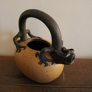 May include: A brown teapot with a black dragon handle and spout. The teapot has a speckled brown glaze and a round body.
