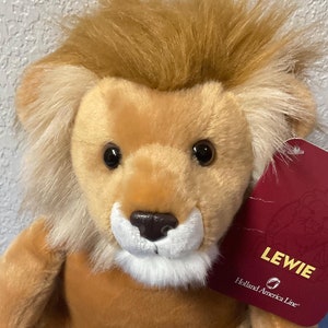 May include: A plush brown lion with a white chest and a blue tag that says "Lewie Holland America Line".