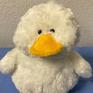 Op de afbeelding: Witte pluche eend met een gele snavel en poten. De eend heeft zwarte ogen en een pluche wit lichaam.
