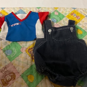 May include: A blue and red short-sleeved shirt with the word "CPIC" on the front, and a pair of blue denim dungarees.