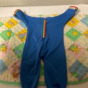 May include: A blue baby onesie with rainbow trim on the sleeves and a rainbow zipper down the back.