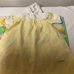Könnte beinhalten: Ein gelbes Babykleid mit weißen Spitzenbesatz und einem weißen Kragen. Das Kleid hat ein kleines Etikett mit der Aufschrift "Carter's".