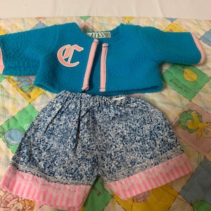 May include: A blue and pink doll outfit with a blue denim skirt and a blue sweater with a pink C on the front.